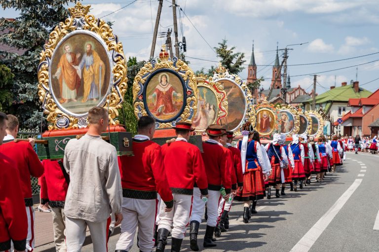 Uczestnicy procesji Bożego Ciała w Myszyńcu w strojach kurpiowskich niosą bogato zdobione obrazy religijne w złoconych ramach ulicą miasta.