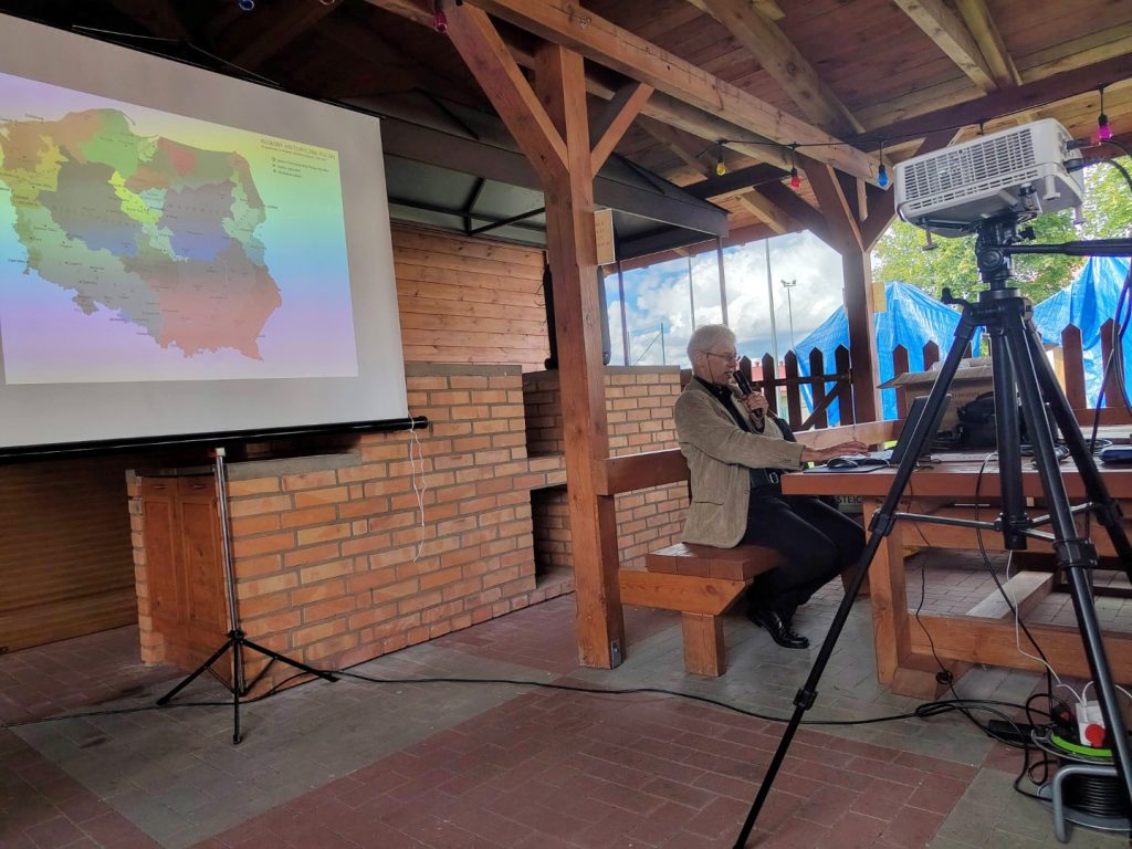 Dr inż. arch. Włodzimierz Witkowski podczas prezentacji, obok ekran z mapą regionów historycznych Polski.