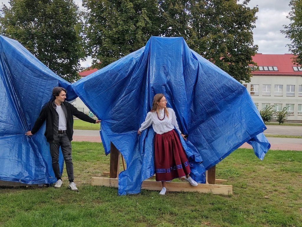 Łucja Samorajczyk i mężczyzna zdejmują niebieskie osłony z drewnianych konstrukcji z etnotablicami.