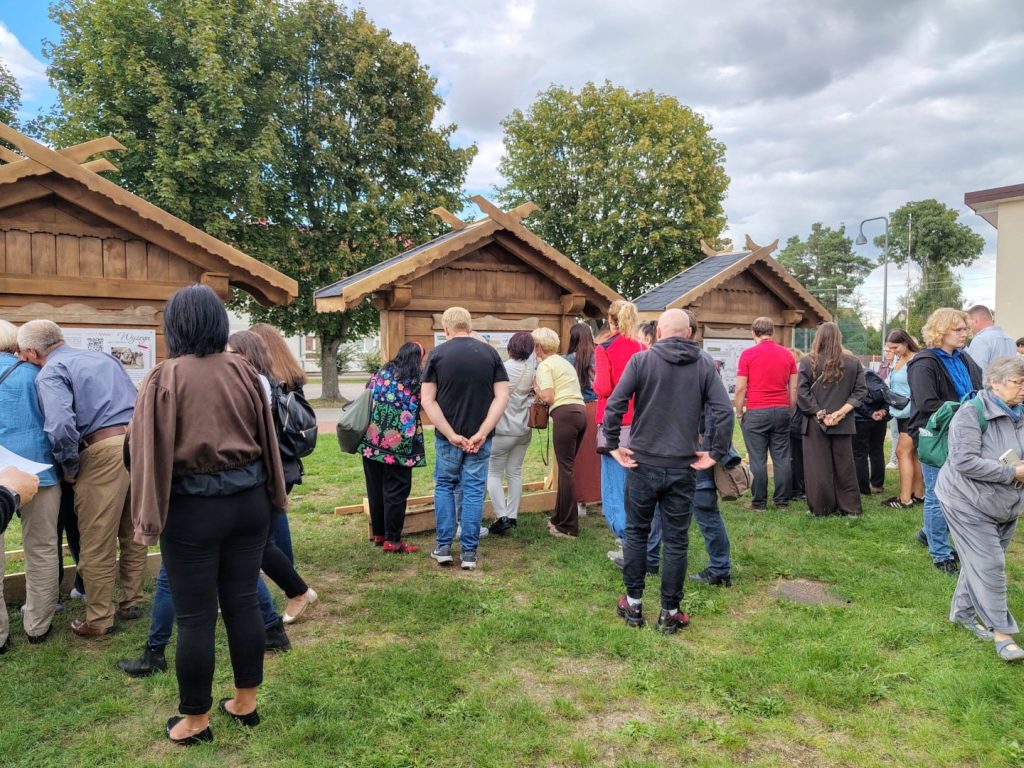 Grupa uczestników ogląda kilka drewnianych etnotablic ustawionych na terenie wydarzenia w Łysych.