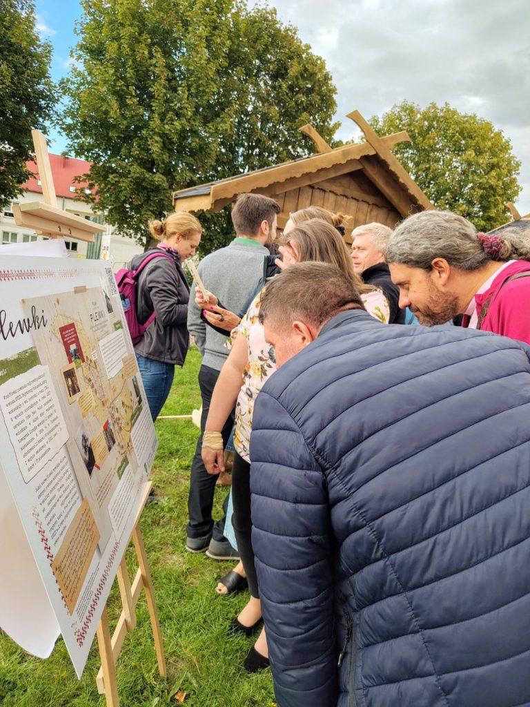 Uczestnicy wydarzenia pochylają się nad planszą z opisem jednej z miejscowości Kurpiowszczyz